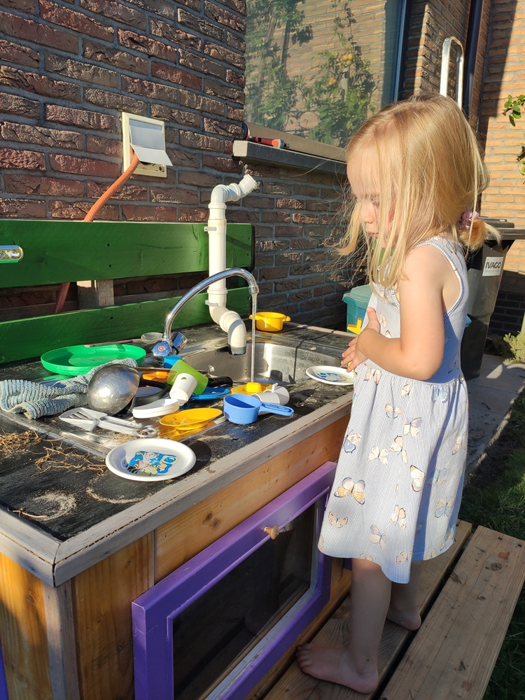 modderkeukentje met speelgoed en spelend meisje